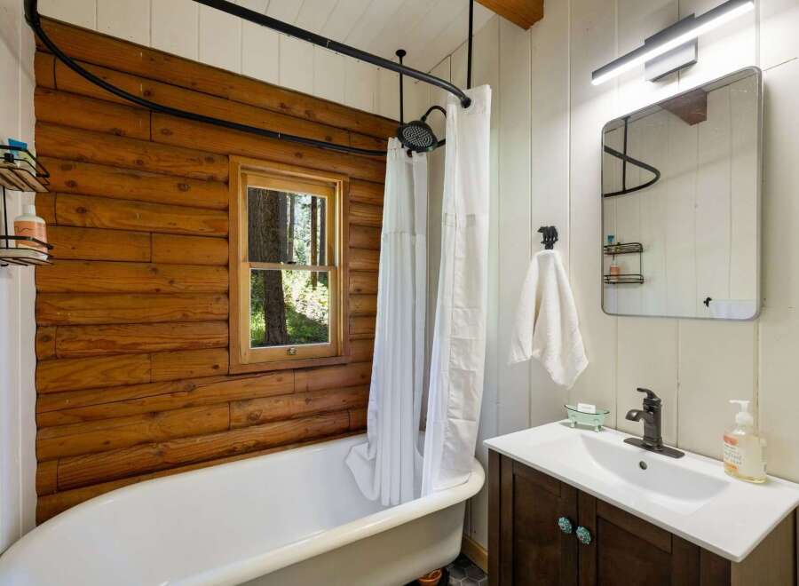 Experience rustic charm in this bathroom featuring a clawfoot tub set against a warm log accent wall.