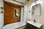 Experience rustic charm in this bathroom featuring a clawfoot tub set against a warm log accent wall.