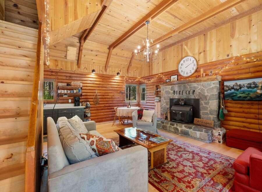 Experience rustic charm in this cozy log cabin living room, featuring a grand stone fireplace and a vaulted wood-paneled ceiling adorned with twinkling lights.