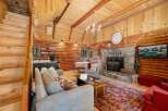Experience rustic charm in this cozy log cabin living room, featuring a grand stone fireplace and a vaulted wood-paneled ceiling adorned with twinkling lights.