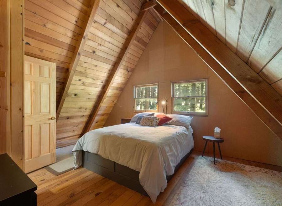 Discover cozy cabin living in this charming attic bedroom, featuring a comfortable bed nestled under a sloped wooden ceiling.