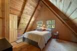 Discover cozy cabin living in this charming attic bedroom, featuring a comfortable bed nestled under a sloped wooden ceiling.