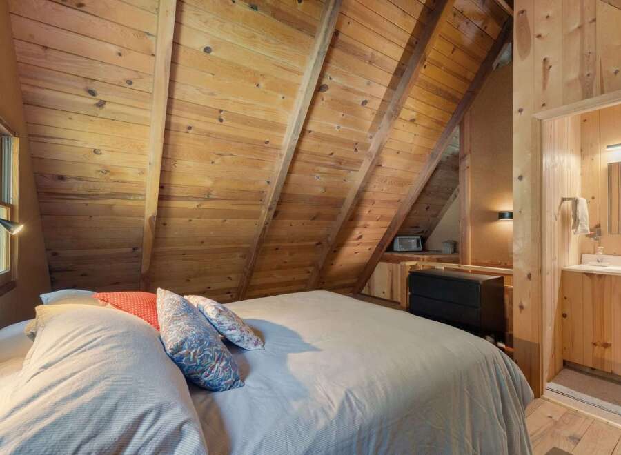 Experience cozy cabin living in this charming bedroom featuring a sloped wooden ceiling and a comfortable bed adorned with decorative pillows.