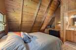 Experience cozy cabin living in this charming bedroom featuring a sloped wooden ceiling and a comfortable bed adorned with decorative pillows.