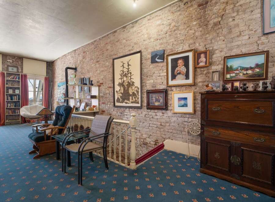 Exposed brick walls add rustic charm to this inviting living space, complemented by a cozy reading nook featuring a plush papasan chair and a rocking chair.