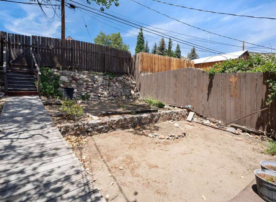Discover the potential of this unique backyard space, featuring a rustic stone retaining wall and a charming wooden boardwalk leading to elevated stairs.