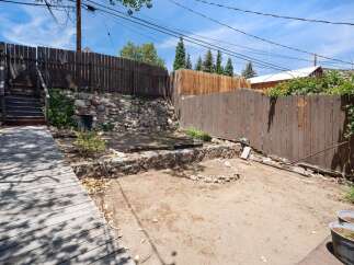 Discover the potential of this unique backyard space, featuring a rustic stone retaining wall and a charming wooden boardwalk leading to elevated stairs.