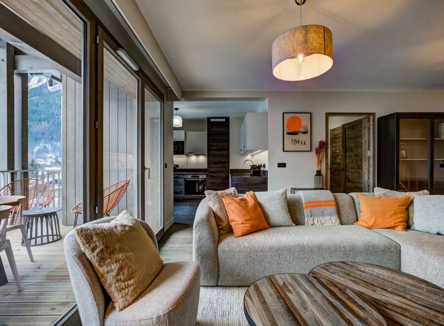 Experience breathtaking mountain views from this stunning living space, featuring a comfortable sectional sofa adorned with vibrant orange accents and a cozy throw blanket.