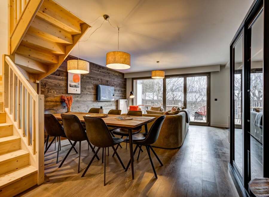Experience modern mountain living in this stunning open-plan space, featuring a rustic wood-paneled accent wall and a cozy dining area perfect for gathering.