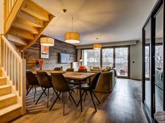 Experience modern mountain living in this stunning open-plan space, featuring a rustic wood-paneled accent wall and a cozy dining area perfect for gathering.