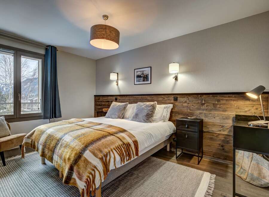 Experience cozy mountain living in this charming bedroom, featuring a comfortable bed adorned with a warm plaid throw and plush pillows.