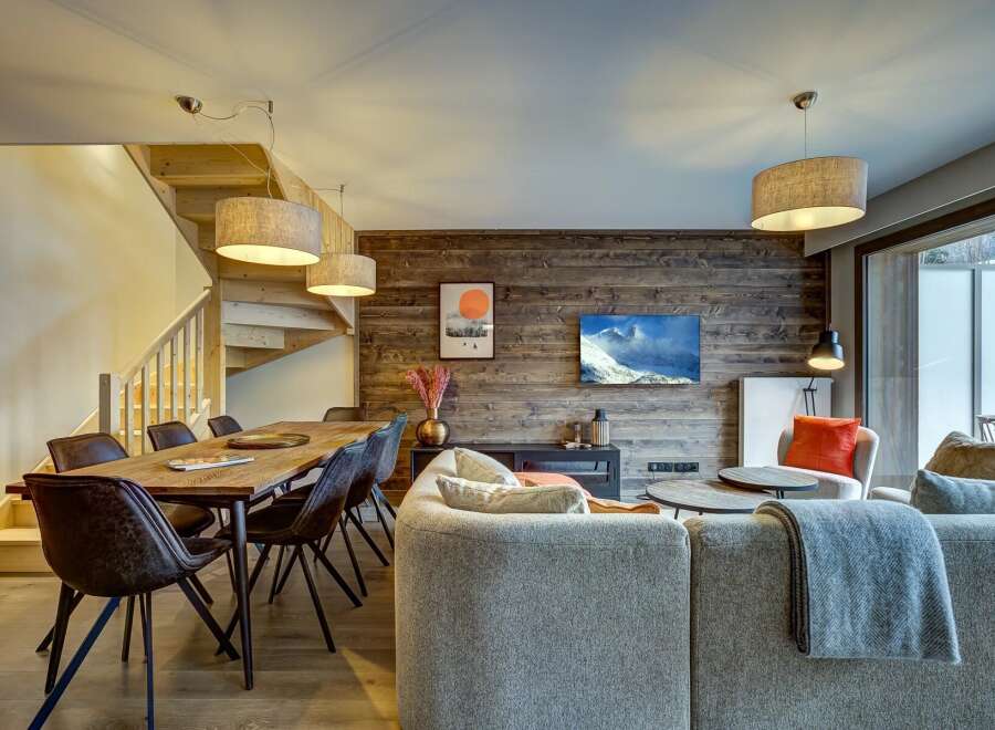Experience modern mountain living in this stunning open-concept space, featuring a rustic wood-paneled accent wall and a cozy living area.