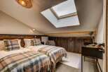 Experience cozy comfort in this charming attic bedroom, featuring two twin beds adorned with plush plaid blankets and matching throw pillows.