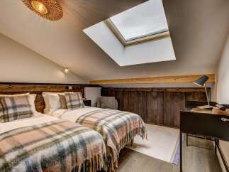 Experience cozy comfort in this charming attic bedroom, featuring two twin beds adorned with plush plaid blankets and matching throw pillows.