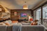 Experience cozy living in this mountain retreat, featuring a warm, wood-paneled living area with a comfortable sectional sofa and a large flat-screen TV.