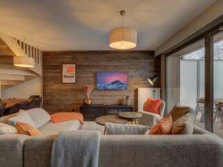 Experience cozy living in this mountain retreat, featuring a warm, wood-paneled living area with a comfortable sectional sofa and a large flat-screen TV.
