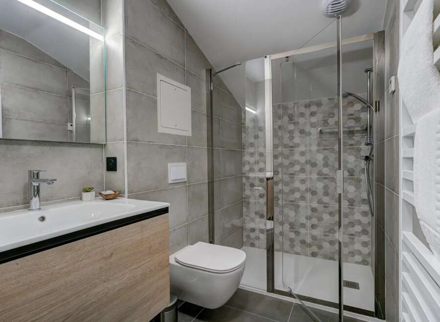 This modern bathroom features a sleek vanity with a vessel sink, a wall-mounted toilet, and a spacious glass-enclosed shower with hexagonal tile accents.