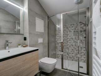 This modern bathroom features a sleek vanity with a vessel sink, a wall-mounted toilet, and a spacious glass-enclosed shower with hexagonal tile accents.