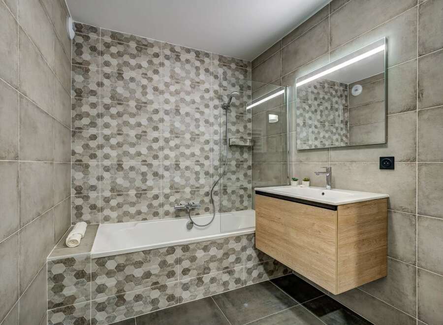 Experience modern comfort in this beautifully designed bathroom, featuring a sleek bathtub with a hexagonal tile accent wall.