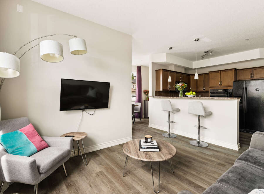 Experience modern living in this open-concept condo featuring a stylish living area with a wall-mounted TV and a comfortable armchair.