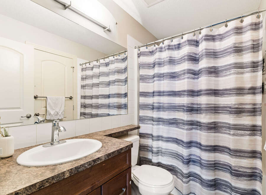 This bathroom features a modern vanity with a granite countertop and a sleek chrome faucet, complemented by a large mirror reflecting the space.