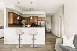 This modern kitchen features rich wood cabinetry, a granite countertop breakfast bar with two stylish stools, and sleek stainless steel appliances.