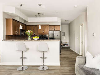 This modern kitchen features rich wood cabinetry, a granite countertop breakfast bar with two stylish stools, and sleek stainless steel appliances.