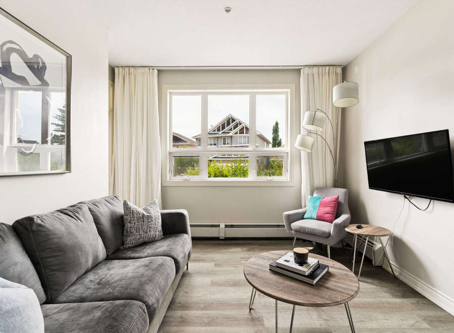 Experience modern living in this stylish apartment, featuring a comfortable grey sofa and a chic accent chair adorned with vibrant pillows.