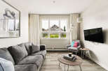 Experience modern living in this stylish apartment, featuring a comfortable grey sofa and a chic accent chair adorned with vibrant pillows.
