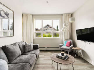Experience modern living in this stylish apartment, featuring a comfortable grey sofa and a chic accent chair adorned with vibrant pillows.