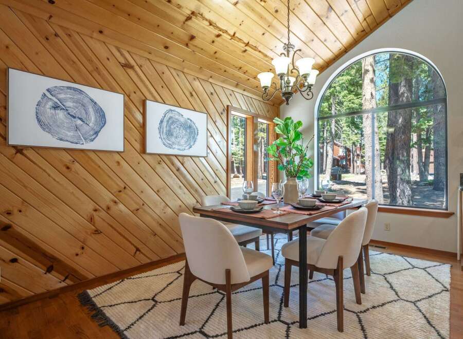 Experience cozy dining in this charming space featuring a rustic wood-paneled accent wall and a large arched window framing a picturesque forest view.