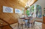 Experience cozy dining in this charming space featuring a rustic wood-paneled accent wall and a large arched window framing a picturesque forest view.