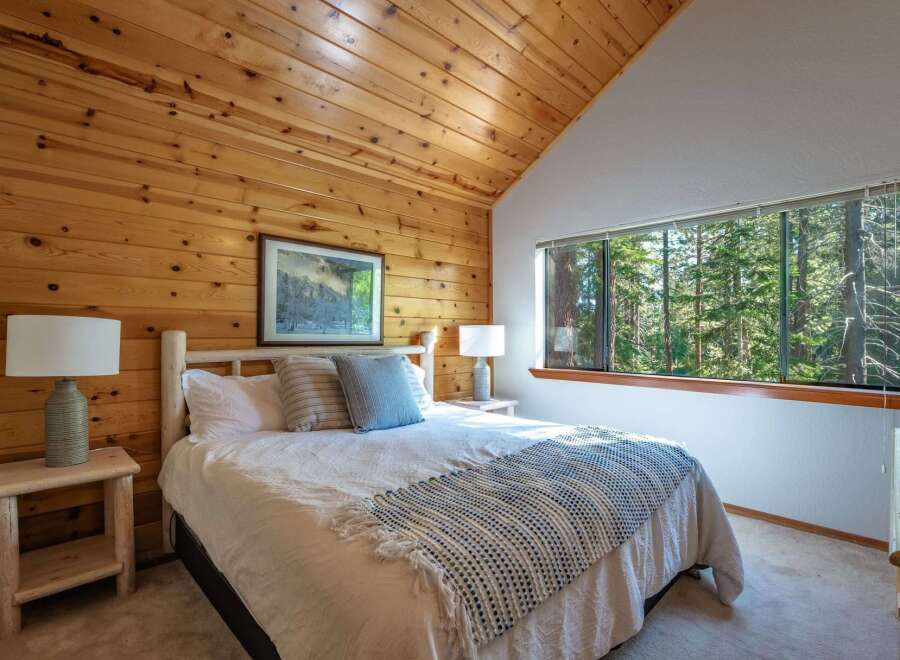 Experience rustic charm in this cozy bedroom, featuring warm wood-paneled walls and a vaulted ceiling.