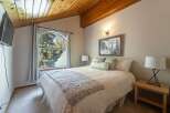 Experience cozy mountain living in this charming bedroom featuring a vaulted wood-paneled ceiling and a large arched window offering picturesque forest views.