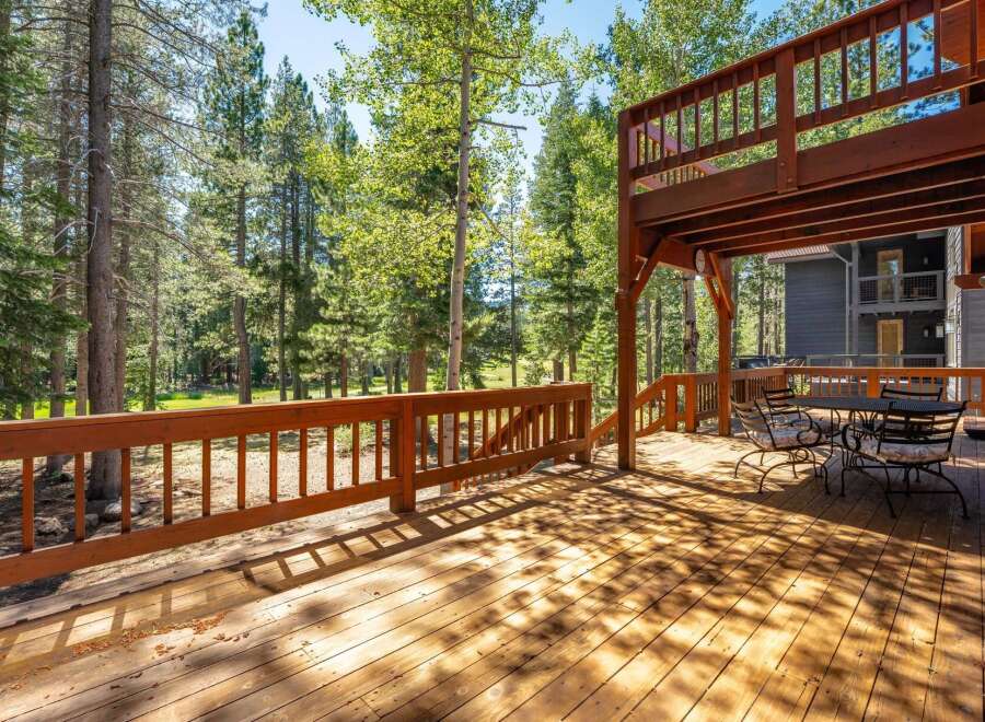 Enjoy the serene mountain lifestyle from this expansive wooden deck, perfect for outdoor dining and relaxation amidst a backdrop of tall pine trees.