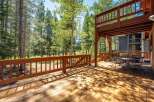 Enjoy the serene mountain lifestyle from this expansive wooden deck, perfect for outdoor dining and relaxation amidst a backdrop of tall pine trees.