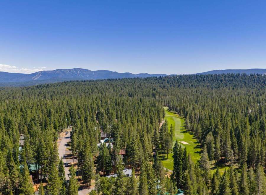 Experience the ultimate mountain lifestyle with this stunning aerial view showcasing a beautiful golf course nestled amidst a dense pine forest.