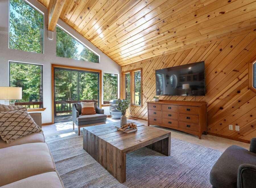 Experience rustic charm in this inviting living room, featuring a vaulted wood-paneled ceiling and a large stone fireplace.