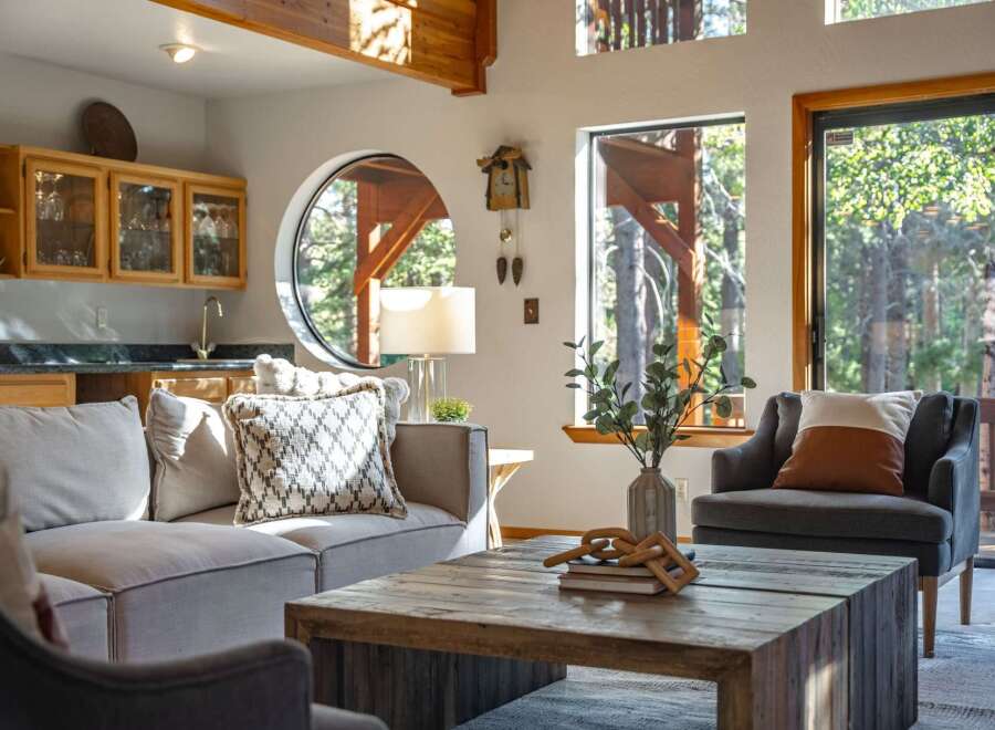 Experience rustic charm and modern comfort in this inviting living space, featuring a cozy sectional sofa and a unique circular window framing forest views.