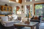 Experience rustic charm and modern comfort in this inviting living space, featuring a cozy sectional sofa and a unique circular window framing forest views.