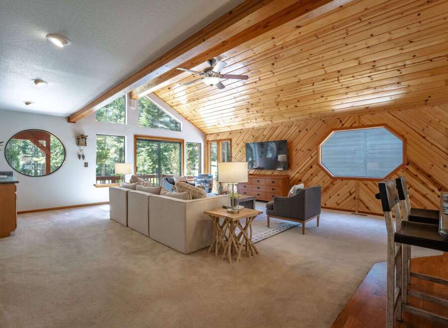 Experience rustic charm in this spacious living area, featuring a vaulted wood-paneled ceiling with exposed beams and a cozy seating arrangement.