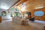 Experience rustic charm and modern comfort in this inviting living room, featuring a vaulted wood-paneled ceiling with a ceiling fan and expansive windows that flood the space with natural light.