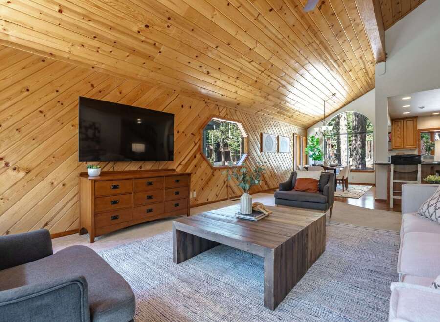 Experience rustic charm in this inviting living space featuring a vaulted wood-paneled ceiling and a large flat-screen TV mounted above a stylish dresser.