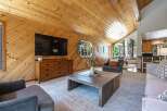 Experience rustic charm in this inviting living space featuring a vaulted wood-paneled ceiling and a large flat-screen TV mounted above a stylish dresser.