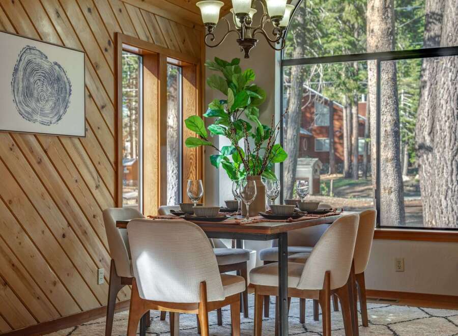 Experience cozy dining in this charming space, featuring a rustic wood-paneled accent wall and a large window offering serene forest views.