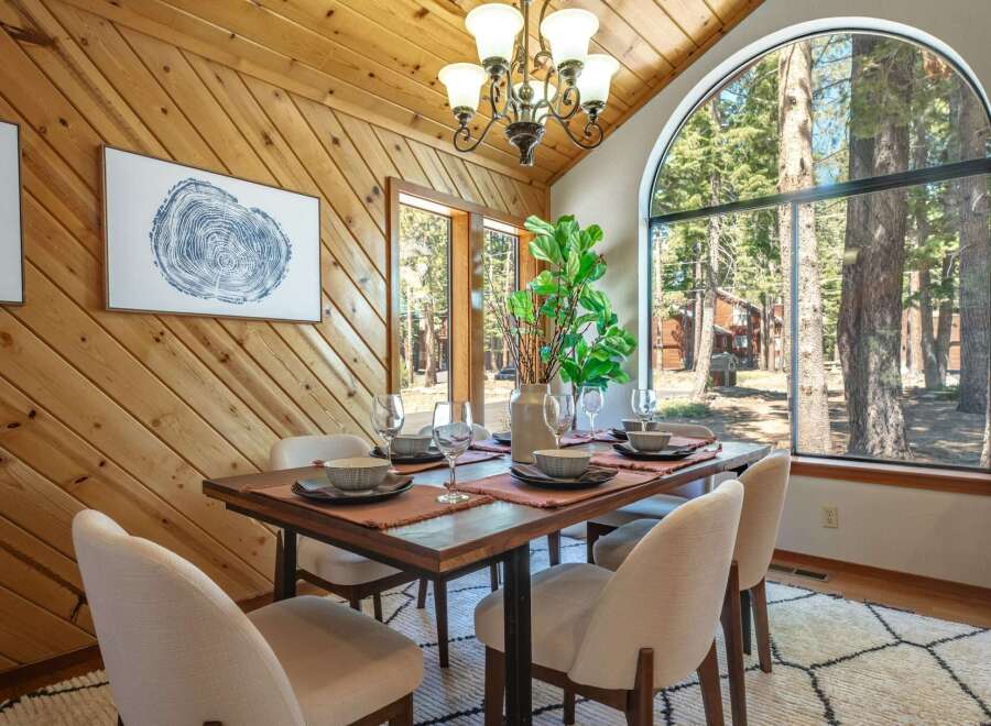 Experience rustic charm in this dining room featuring a large arched window with stunning forest views.