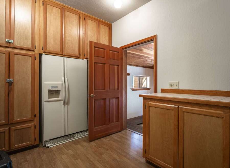 Discover ample storage with this kitchen's extensive wooden cabinetry, featuring a double-door refrigerator and a convenient built-in water dispenser.