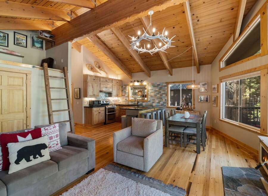 Experience rustic charm in this open-concept living space, featuring a vaulted wood-beamed ceiling and a cozy antler chandelier.