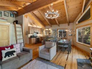 Experience rustic charm in this open-concept living space, featuring a vaulted wood-beamed ceiling and a cozy antler chandelier.