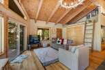Experience rustic charm in this cozy living room featuring a vaulted wood-paneled ceiling with exposed beams and a unique antler chandelier.